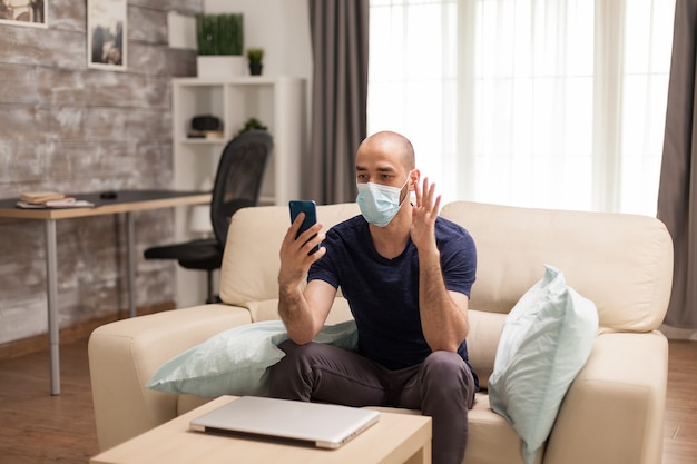 Guy waving during a video call on smartphone in time of global pandemic.