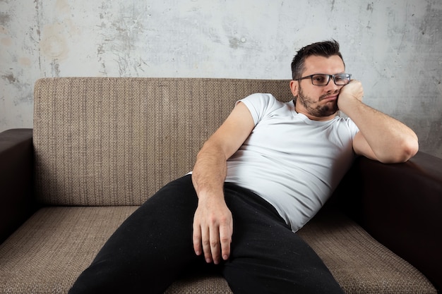 Photo guy wearing a white shirt is lying on the couch.