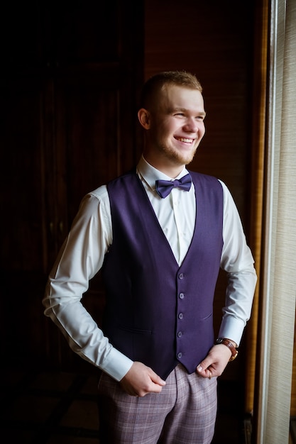 A guy in a white shirt and trousers dresses on a wedding day.