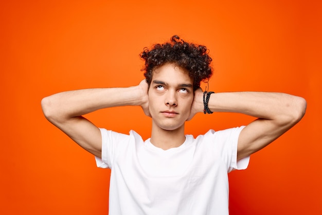 Guy in a white tshirt with curly hair holding his head emotions orange background