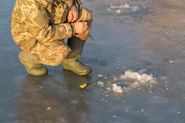 The guy on the winter fishing at the hole catches a small\
fishing pole