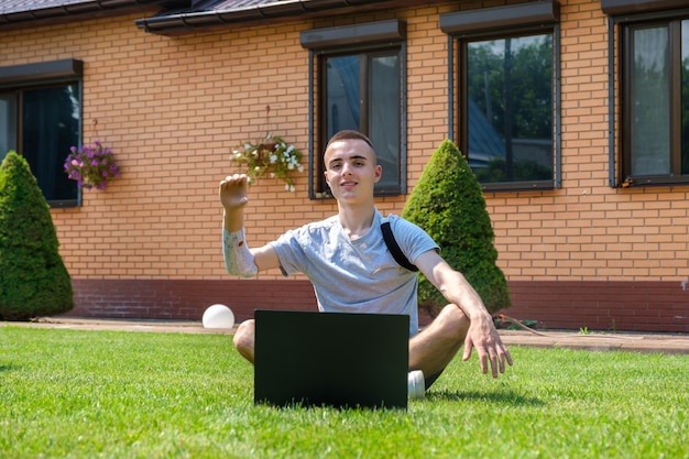 Guy with amputated arm sits on lawn and using laptop