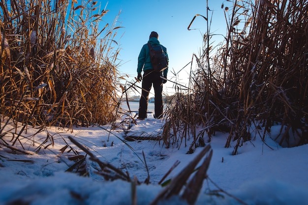 The guy with the backpack is standing at the frozen lake and looking ahead.