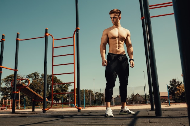 Guy with a beautiful athletic body posing while standing next to the horizontal bars