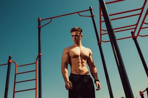 Guy with a beautiful athletic body posing while standing next to the horizontal bars