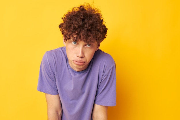 Guy with curly hair in purple tshirts studio yellow background