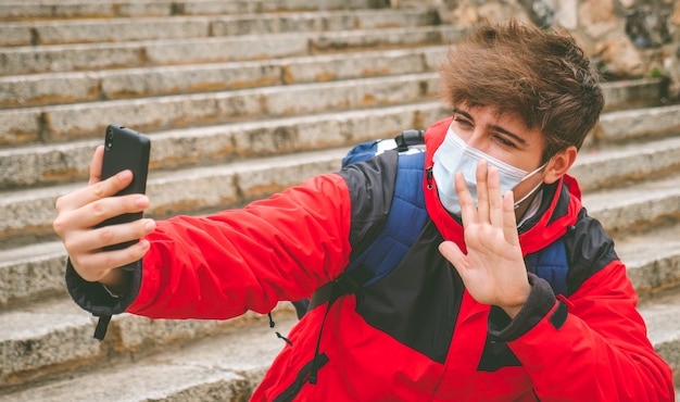 冬の日に通りの階段で自分撮りをしているフェイスマスクとバックパックを持つ男