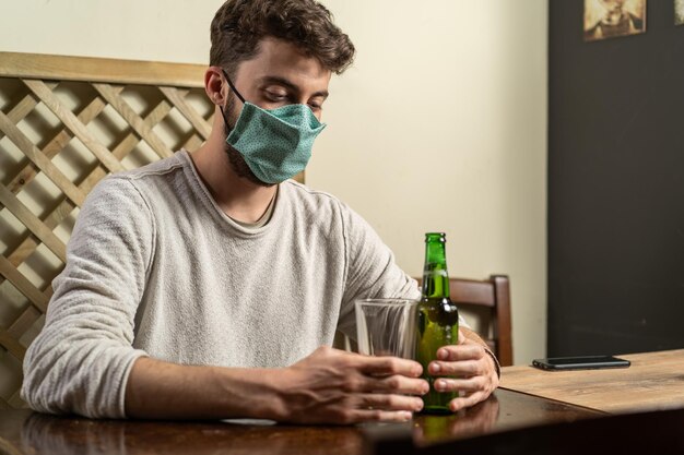 Guy with fashion face mask drinking beer alone in a indoor pub new normal concept