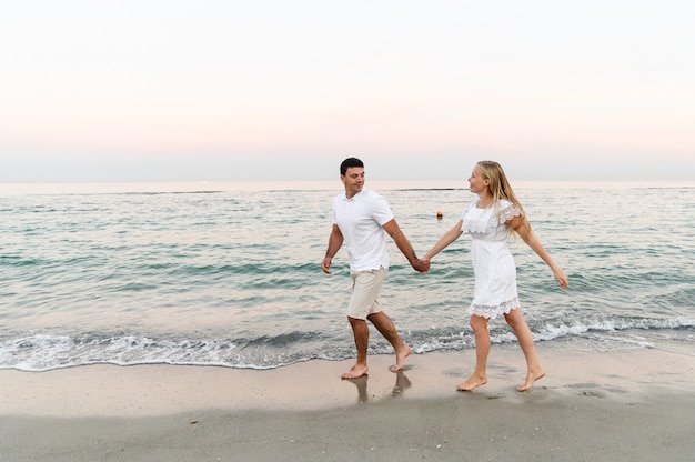 夏服を着た女の子と一緒に海を歩いている男。海の近くの日のロマンチックな夕日で夫と妻。