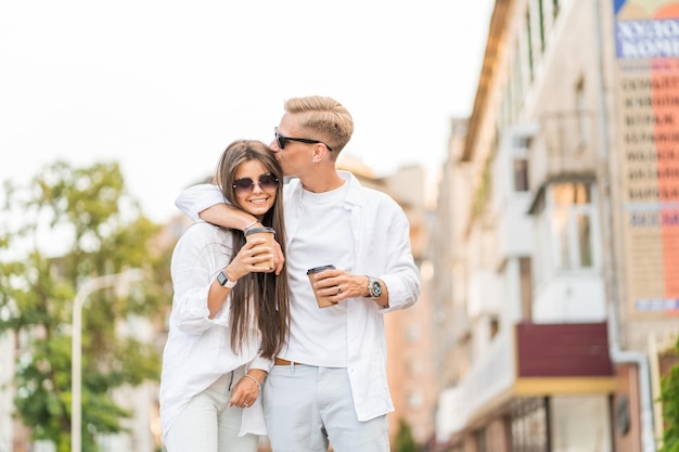 Guy with a girl in white clothes walks around the city and drinks coffee