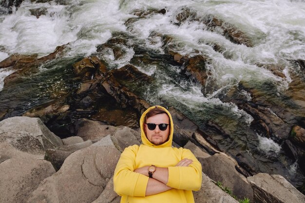 A guy with glasses lying on top of a rock in the summer mountains near a mountain river