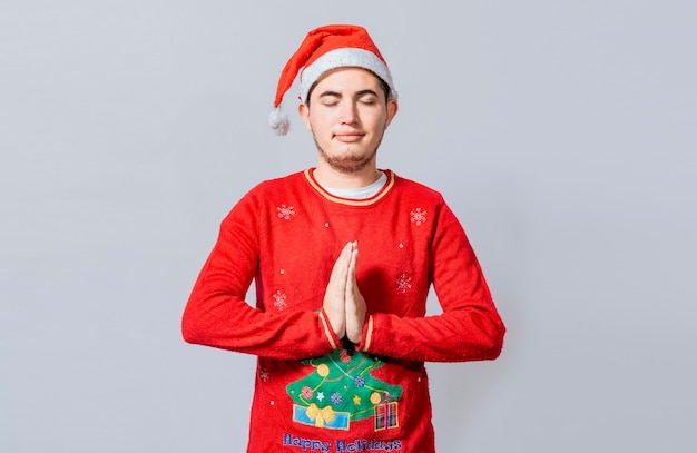Guy with hands together praying in christmas isolated concept of person with christmas hat praying and making a wish Man with christmas hat with praying hands isolated