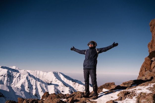 山の冬の風景を背景に腕を広げた男が立っている