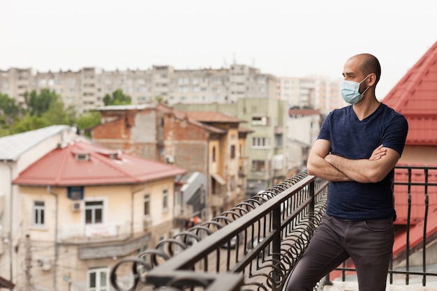 Парень с профилактической маской на балконе квартиры во время глобальной пандемии.