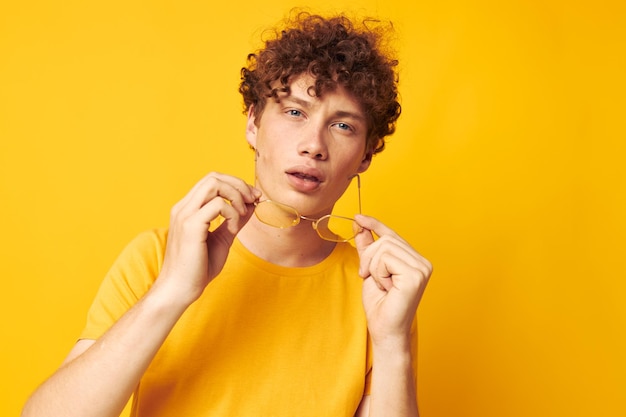 Ragazzo con capelli ricci rossi che indossa una maglietta gialla con occhiali eleganti in posa stile di vita inalterato