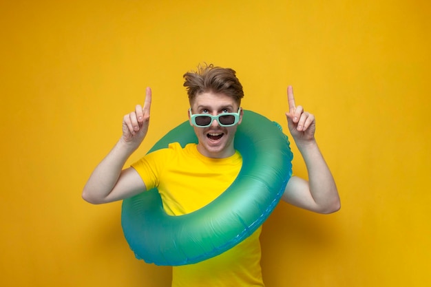 Guy with swimming inflatable ring shows his hands up on yellow background man tourist on vacation