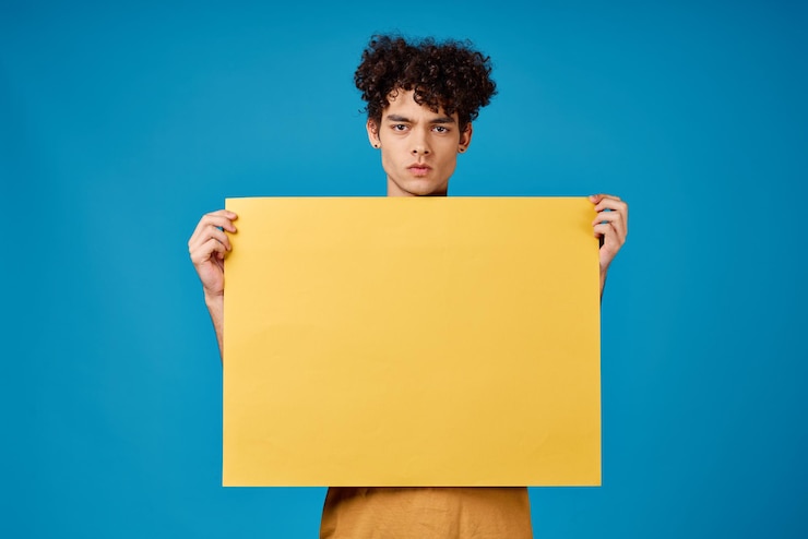 Photo guy with yellow poster in hands copy space advertising blue background high quality photo