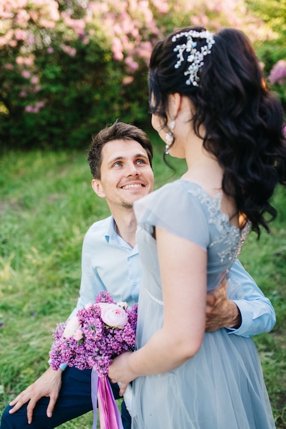 A guy and a woman walk in the spring garden of lilacs before the wedding ceremony