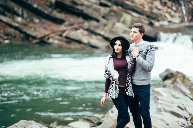 Guy and woman in warm sweaters walking along a mountain river