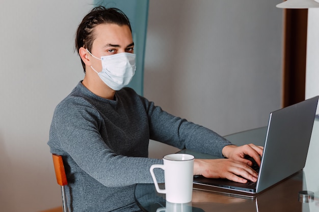 Guy working at home with protective mask on laptop