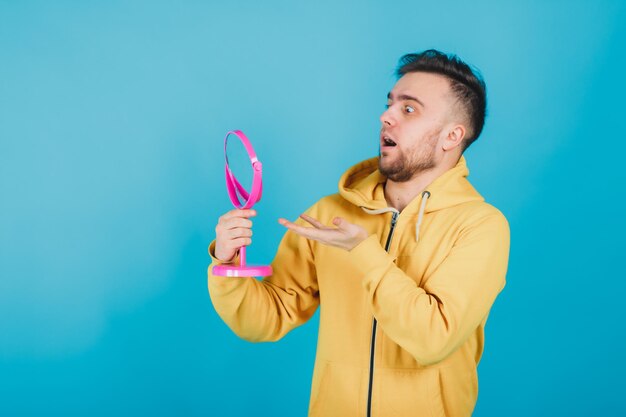 the guy in the yellow sweatshirt looks at himself in the pink mirror