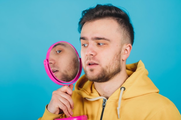 the guy in the yellow sweatshirt looks at himself in the pink mirror