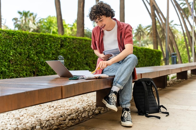 Guy zit buiten op de bank en kijkt naar het laptopscherm, leest en studeert