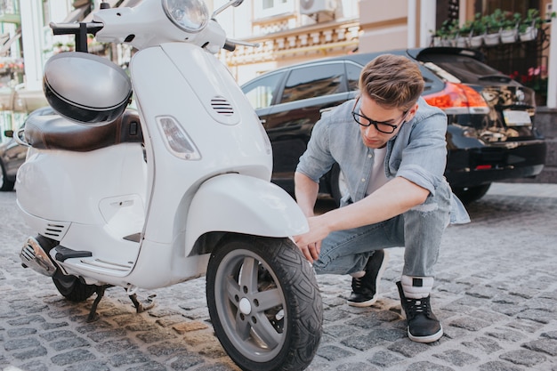 Guy zit in squat positie en kijken naar motorfiets wiel