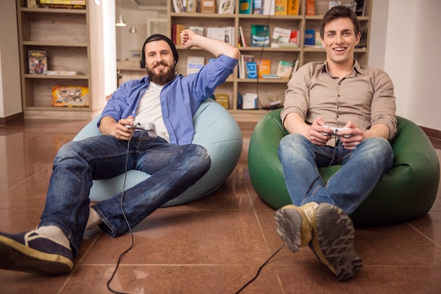 Guys sitting on poufs and playing video games together.