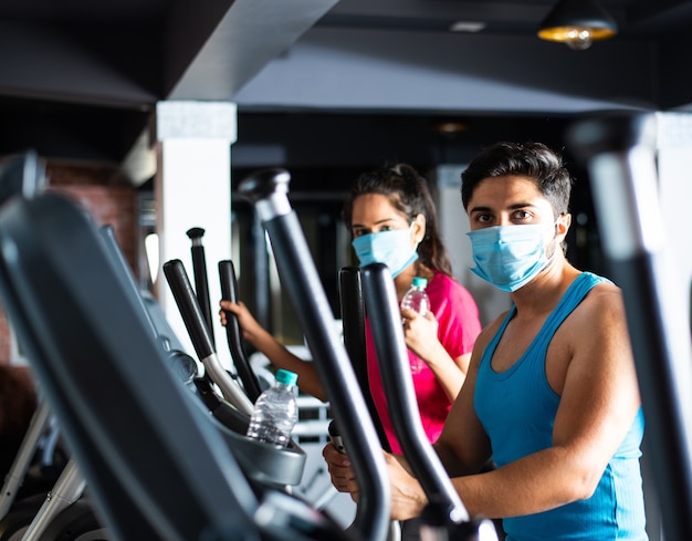 Gym after corona - Indian young couple working out in gym post corona outbreak, wears protective face mask