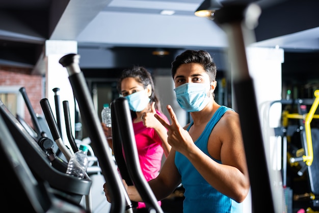 Gym after corona - Indian young couple working out in gym post corona outbreak, wears protective face mask