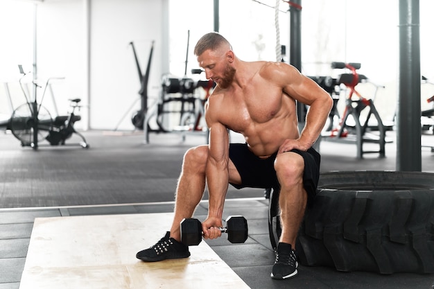 ジムアスリート上腕二頭筋運動ダンベル筋肉質の男性は、リフトバーベルを保持しているホイールに座ります。