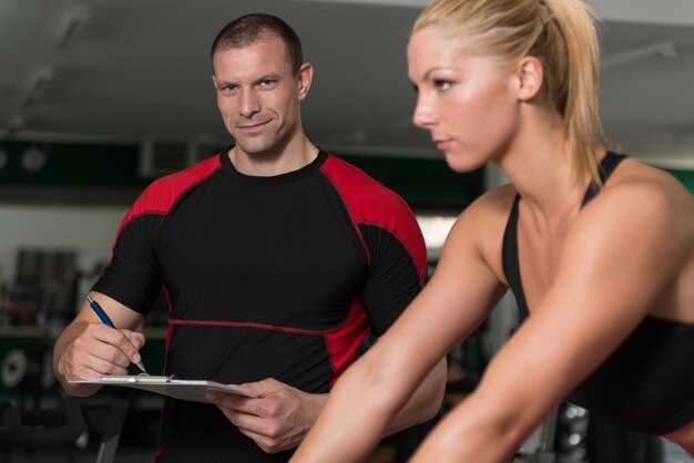 Foto allenatore di palestra che aiuta la donna sulla bicicletta