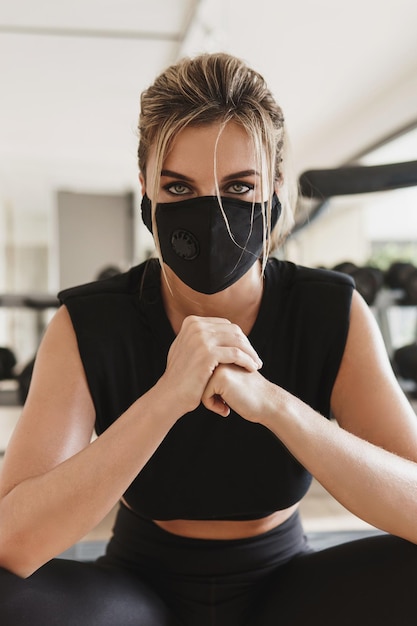 Gym new normal. Young athletic woman wearing a prevention face mask during her fitness workout.