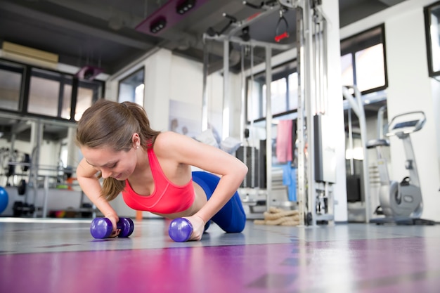 Gym woman doing pushup exercise with dumbbell in a gym