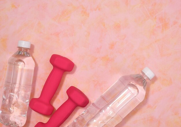 Gym workout en sport concept top view Twee roze dumbbells en plastic flessen met drinkwater Kopieer ruimte voor tekst