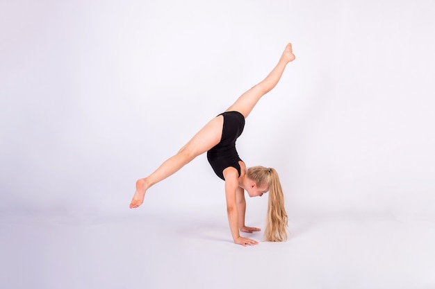 A gymnast performs splits on her hands on a white isolated wall