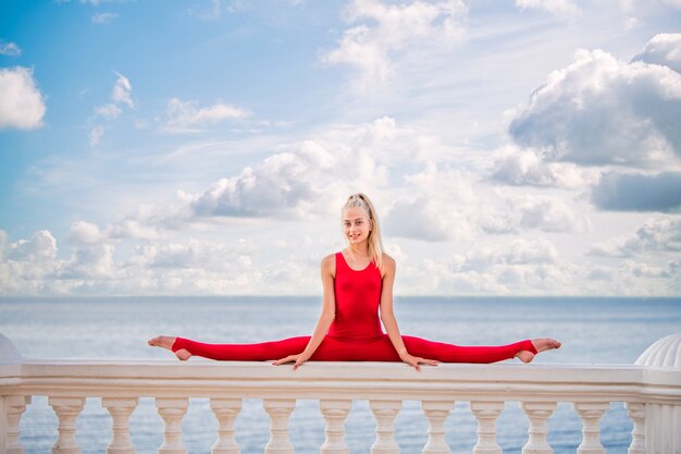 Gymnast teenage girl in a red suit posing on the embankment against the background of the sea and sky