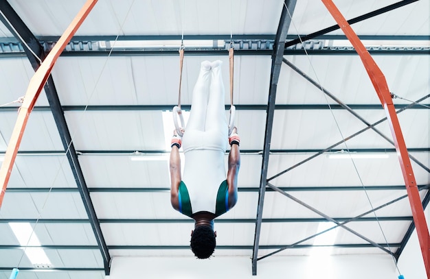 Gymnastics rings and man at gym for fitness workout and body performance or training Balance exercise and guy acrobat at sports studio for athletics resilience and cardio hanging or endurance