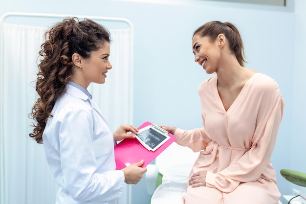 Gynaecoloog toont een foto met echografie aan een jonge vrouwelijke patiënt die de kenmerken van de gezondheid van vrouwen uitlegt tijdens een medisch consult op kantoor