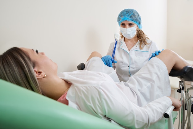 Ginecologo che prepara per una procedura di esame per una donna seduta su una sedia ginecologica