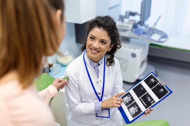 산부인과 의사는 사무실에서 진료를 받는 동안 여성 건강의 특징을 설명하는 젊은 여성 환자에게 초음파 사진을 보여줍니다.