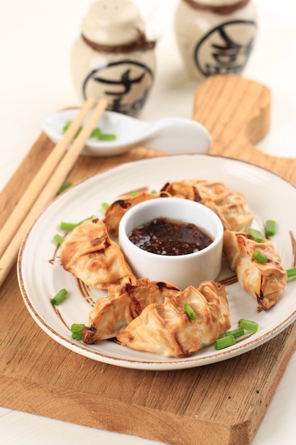 Gyoza азиатские Potstickers с соусами, подаваемые в коричневой керамической тарелке в японском стиле с палочками для еды и весенним луком на белом деревянном фоне. Приготовление пищи в аэрогриле без масла.