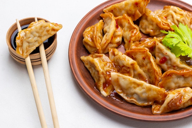 Gyoza dumplings in tomato sauce on ceramic plate Gyoza on chopsticks on bowl with sauce Top view White background
