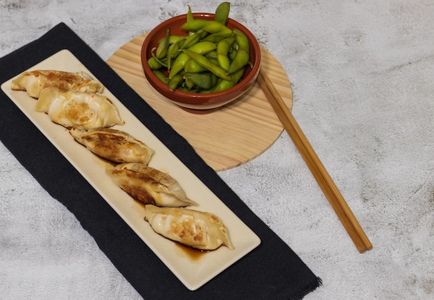 Photo gyozas and edamame on wooden table with chopsticks