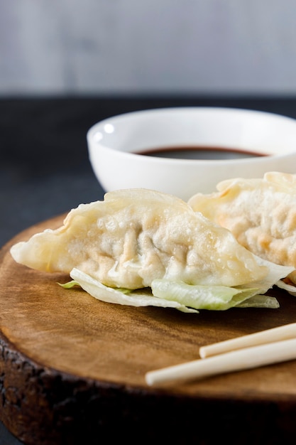 Gyozas geserveerd in zwarte plaat op houten log, met stokjes en zwarte achtergrond