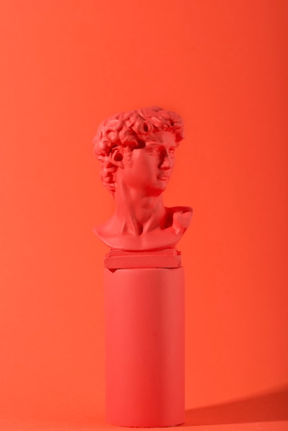 Gypsum bust on coral background with geometric shapes