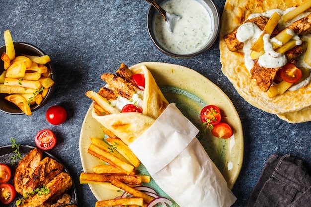 Gyros souvlaki wraps in pita bread with chicken, potatoes and tzatziki sauce, ingredients background.