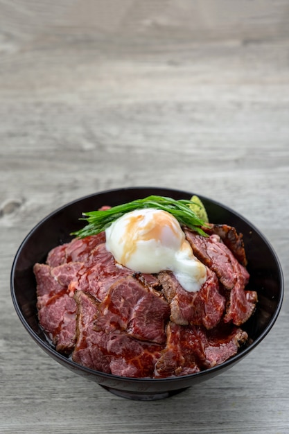 Gyudon raw beef and stream egg serve with rice in blow over the wooden table