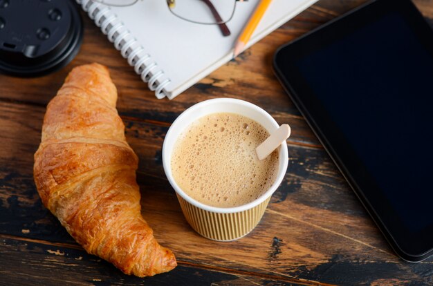 Haal koffiekop met croissant op houten lijst weg.